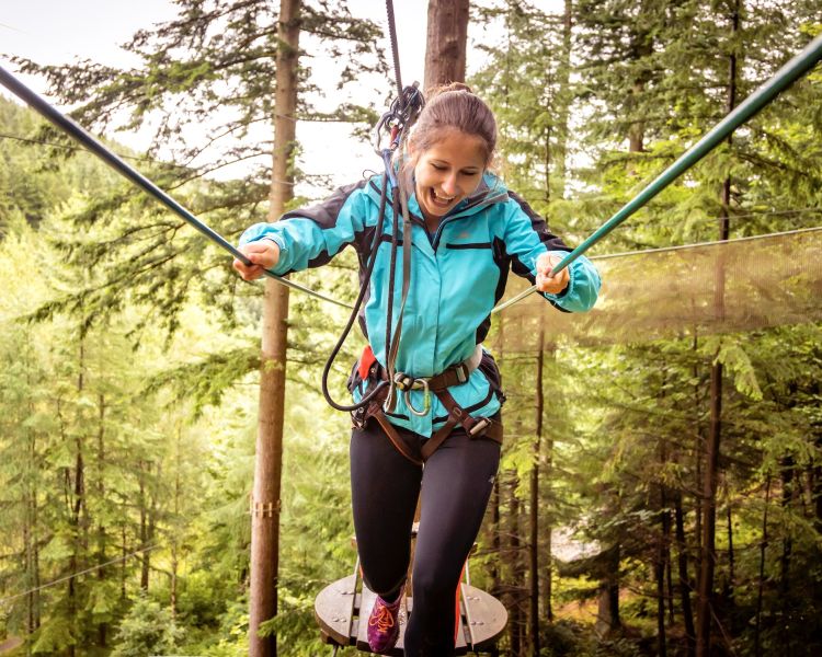 girl walking along treetop challenge course at go ape above trees