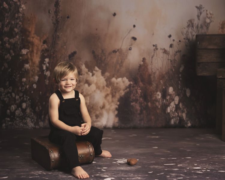 young boy wearing black dungarees sitting on old suitcase on a child photoshoot