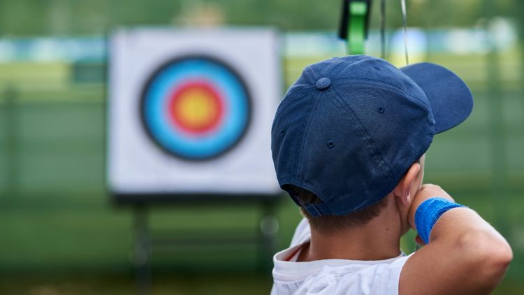 Young boy shoots arrow at target on archery experience