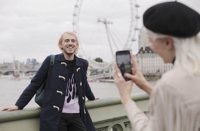 woman taking photo of man with london eye in the background in london on a short break