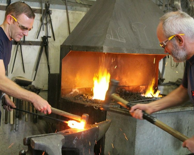 Two men hitting hot metal to make an axe head