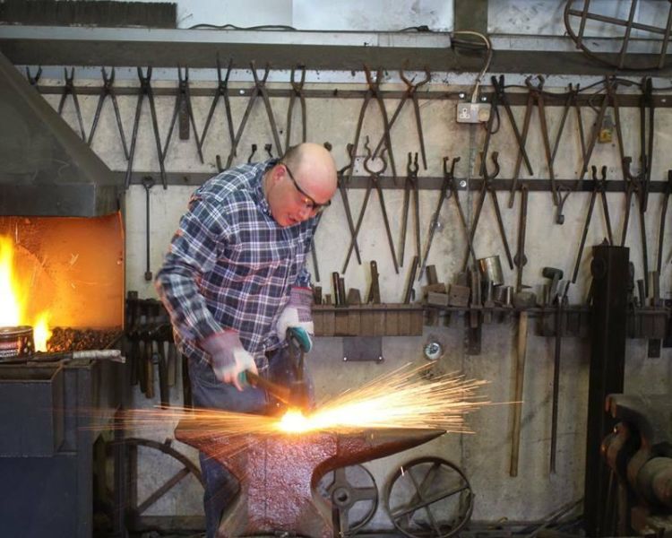 Man hitting hot metal on blacksmith experience