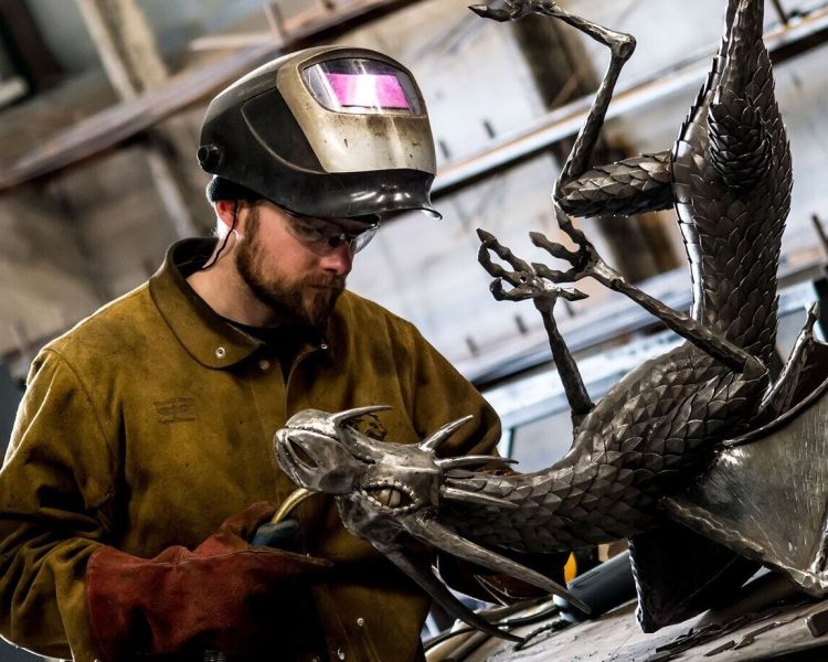 Man welding on a metal dragon sculpture