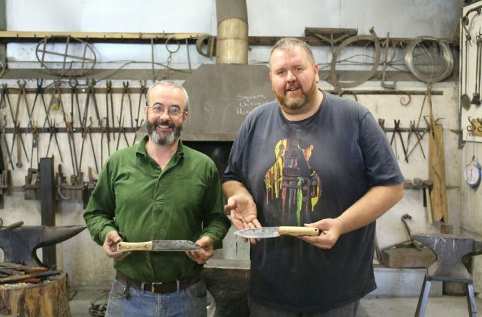 Two men holding knives they have made on a blacksmith experience day