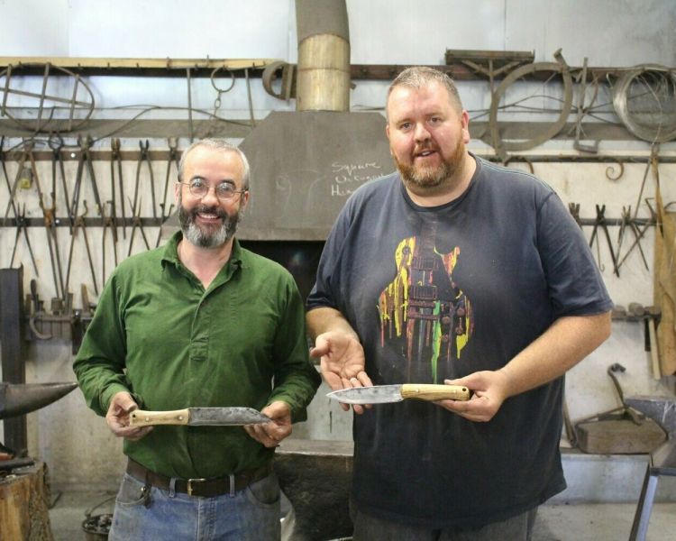 Two men holding knives they have made on a blacksmith experience day
