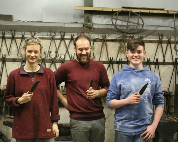 Three people holding knives theyve made on a blacksmith experence day