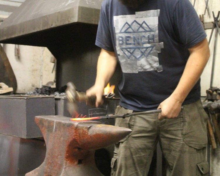 Man hammering hot metal on a knife making experience day