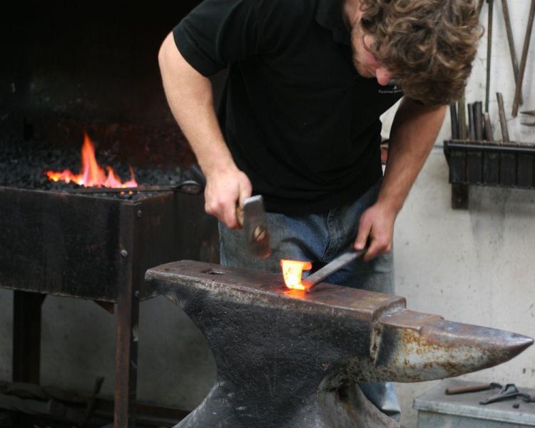 Man hammering hot metal on a tool making blacksmith day