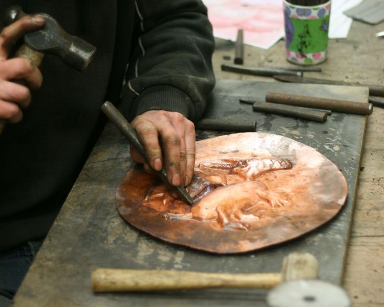 Man hammering design into copper plate on blacksmith course