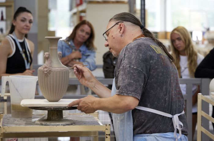 people watching a man decorate a vase on the wedgwood factory tour