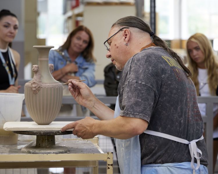 people watching a man decorate a vase on the wedgwood factory tour