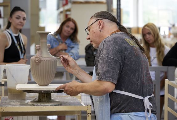 people watching a man decorate a vase on the wedgwood factory tour