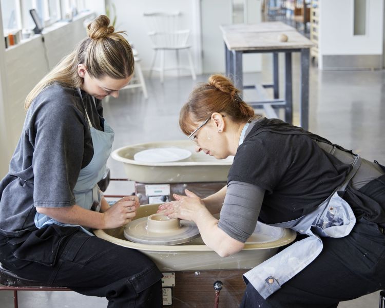 woman being shown how to throw a pot on a wedgwood pottery experience