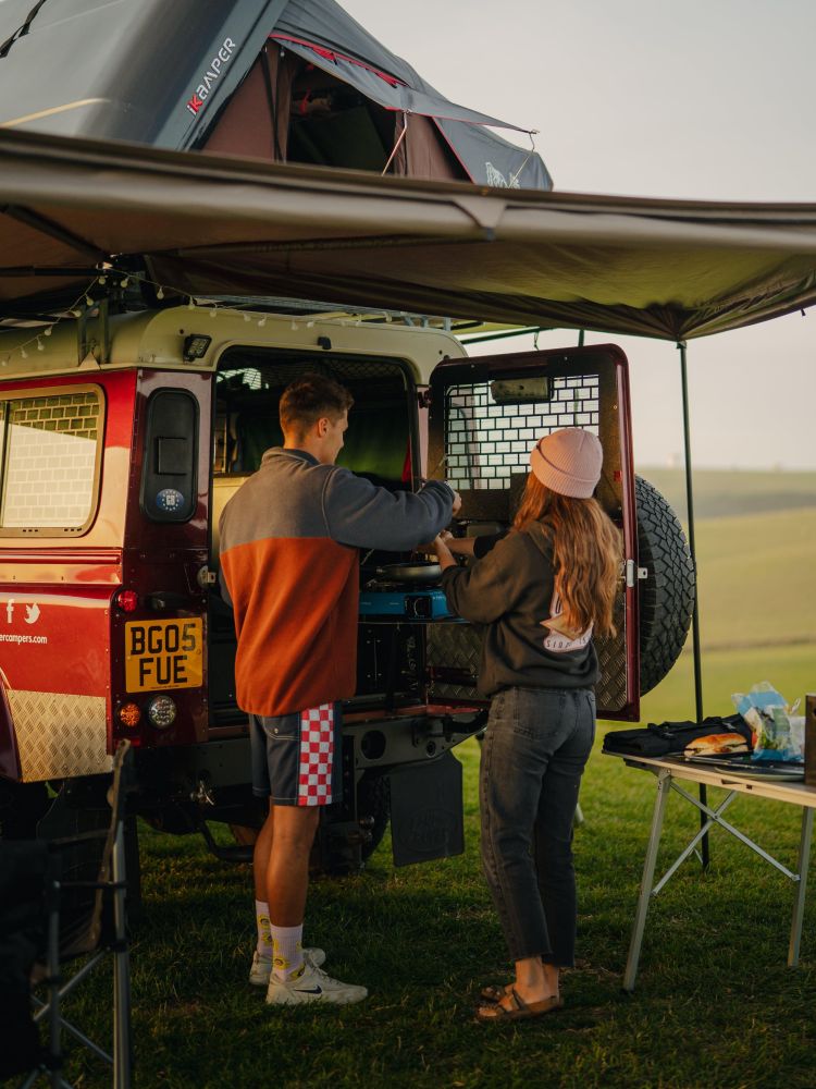 Couple cooking on camping stove in land rover defender campervan