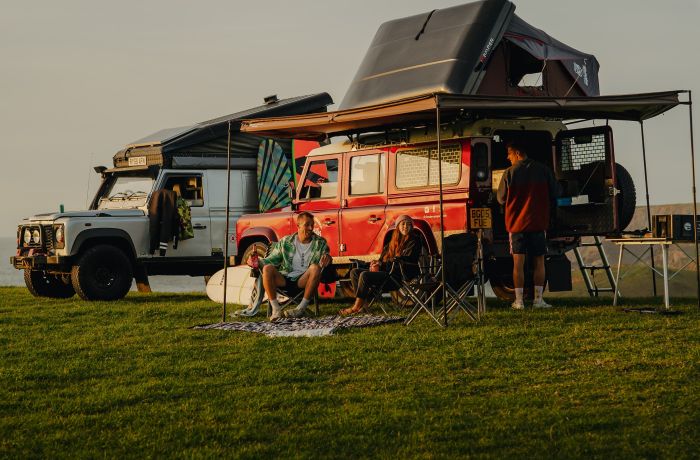 Three people camping in land rover defenders