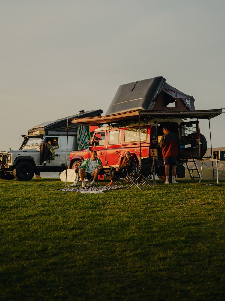 Three people camping in land rover defenders