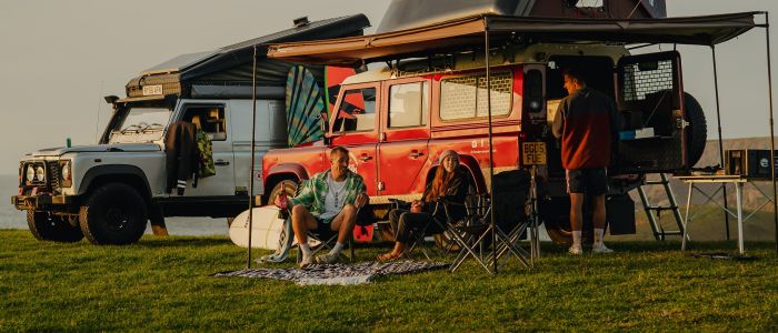 Three people camping in land rover defenders