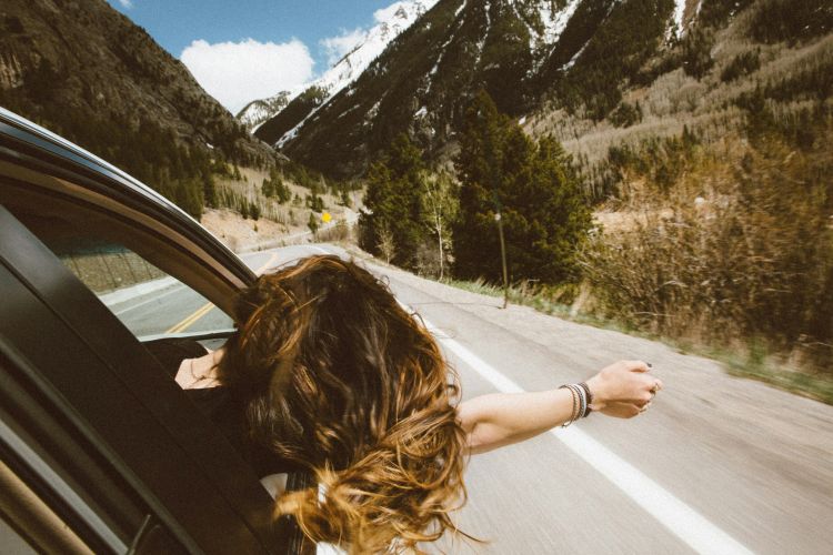 Woman with arm out the car window on a road trip