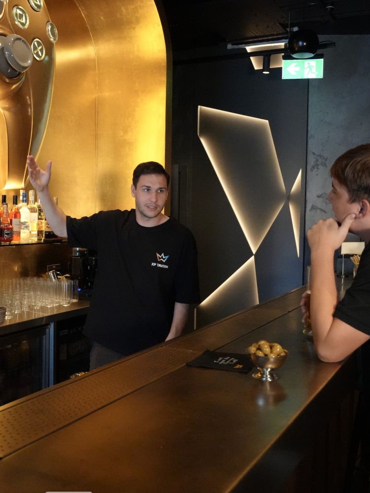 man talking to another behind the bar of a gaming bar in london