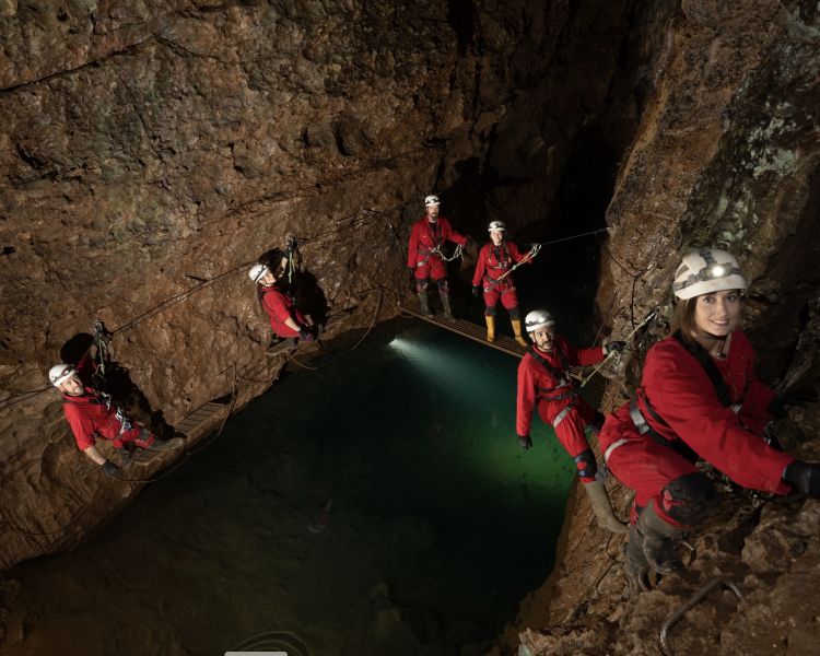 people moving along cave walls with deep pool beneath them