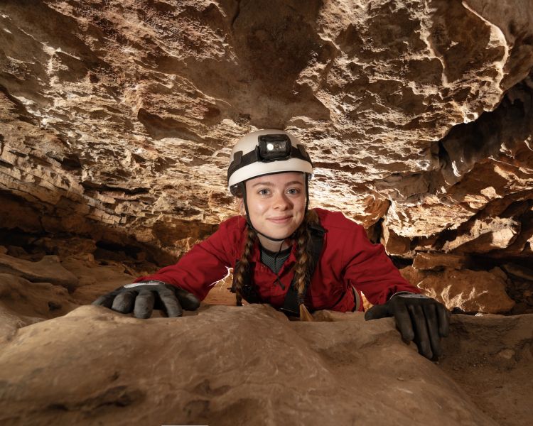 girl moving through cave tunnel on caving experience