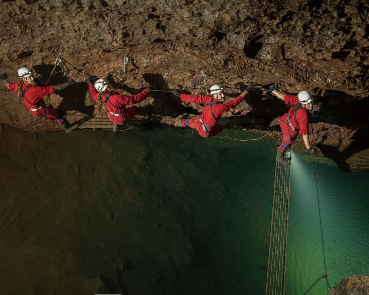 people moving along cave wall above a pool of deep water