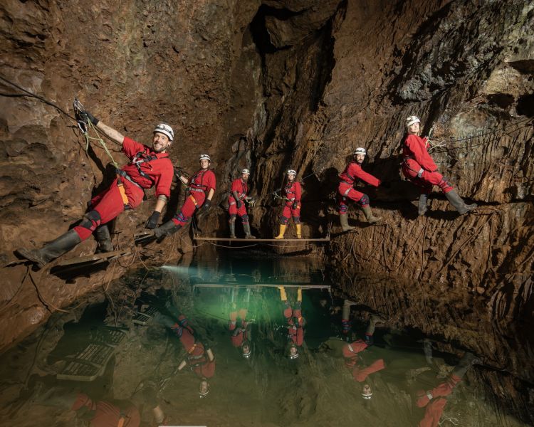group hanging onto cave walls on caving experience with pool of water beneath them