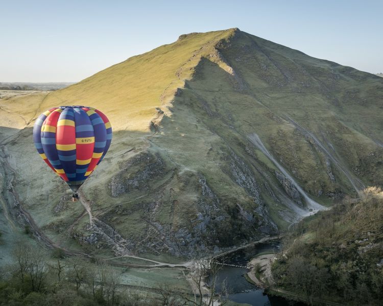 multi-coloured hot air balloon floating over hills and countryside