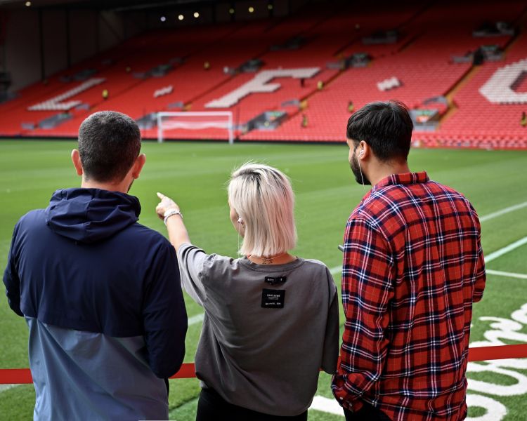 three people looking at the pitch on a liverpool fc stadium tour