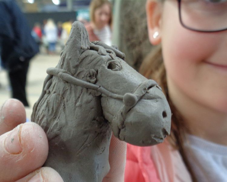 a young girl showing off the horses head she has made on a clay modelling experience day
