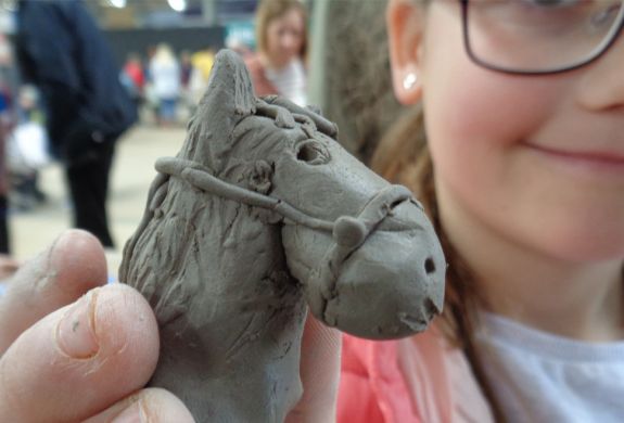 a young girl showing off the horses head she has made on a clay modelling experience day