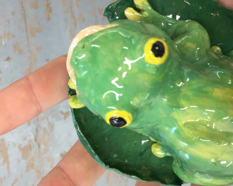 a painted and glazed clay model of a green frog