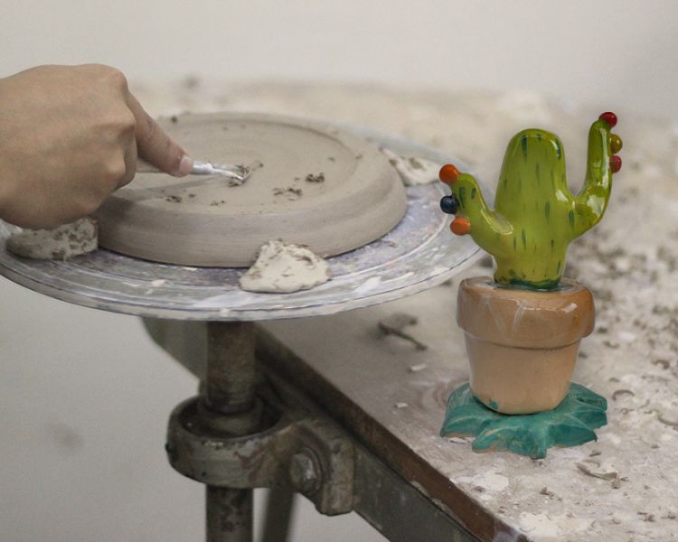 person doing clay modelling at a workbench with a clay cactus model next to them