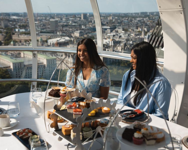 two girls sitting at table for afternoon tea on london eye with london views behind them
