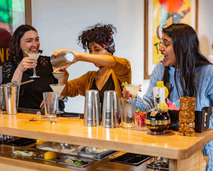 ladies mixing cocktails behind bar station at cocktail class in london